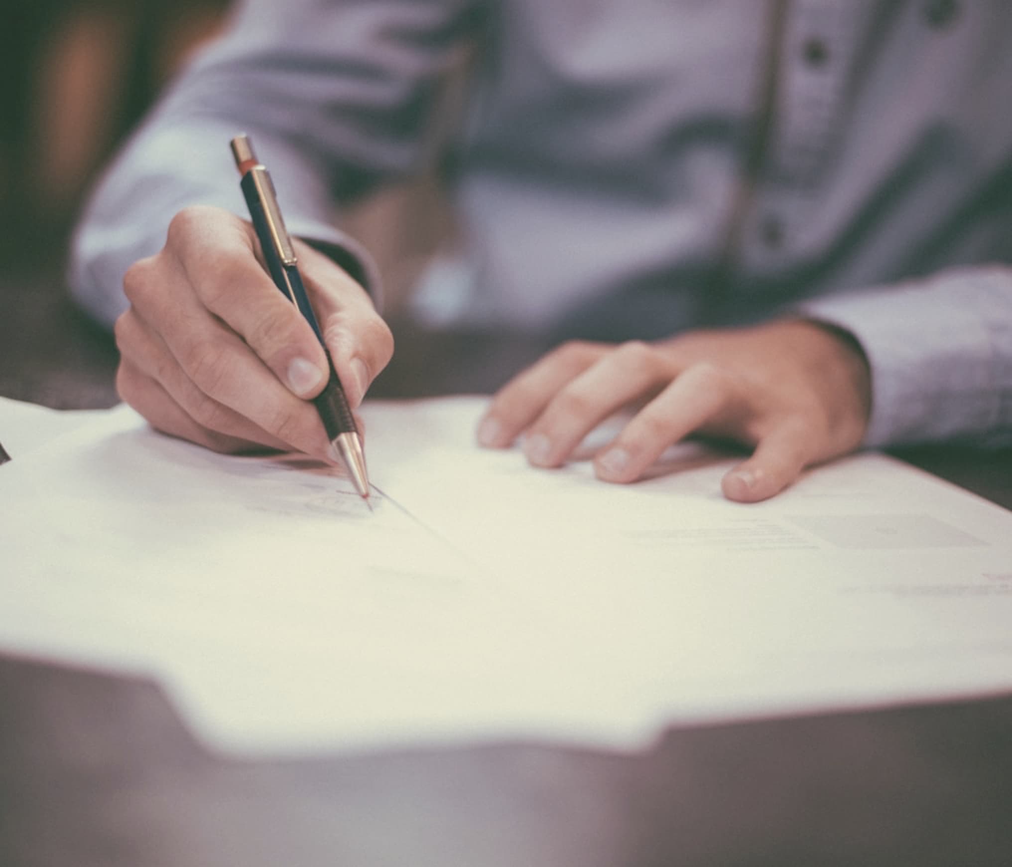 person writing in pen on papers on desk